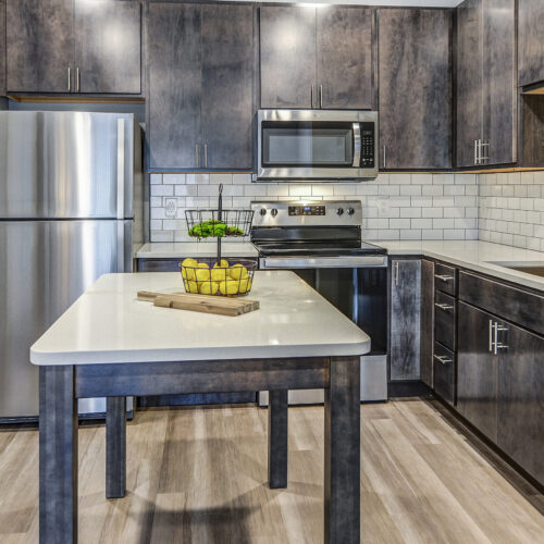 Modern kitchen at Flats at Neill Park, featuring stainless steel appliances, dark wood cabinets, a white subway tile backsplash, and a small island with a bowl of lemons—perfect for those seeking stylish apartments in Burnsville MN.